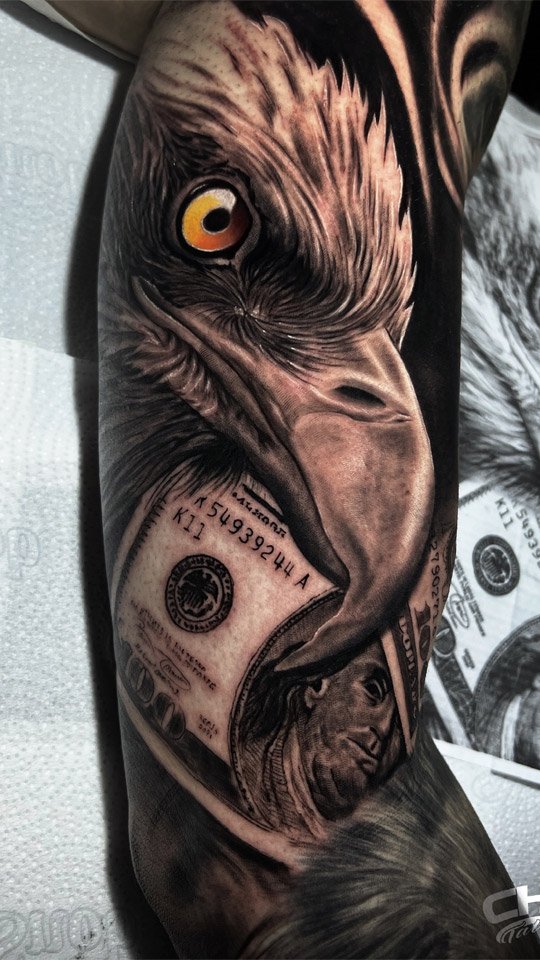 Tatuagem realista de águia com olho âmbar e cédulas de dinheiro, em preto e cinza